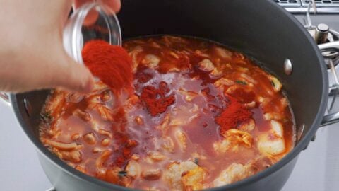 Adding Korean chili powder to a pot of spicy kimchi and pork belly soup.