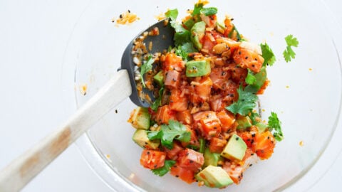 Spicy Salmon Poke in a bowl, with sweet onions, black sesame, avocado, tobiko and a spicy sesame sauce.