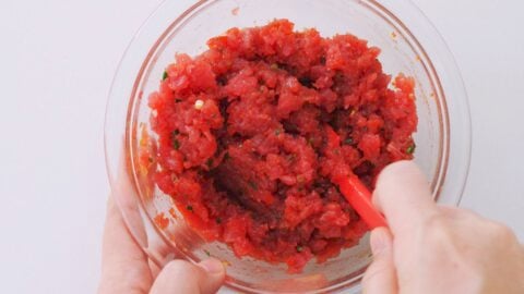 Mixing spicy tuna mixture in a glass bowl.