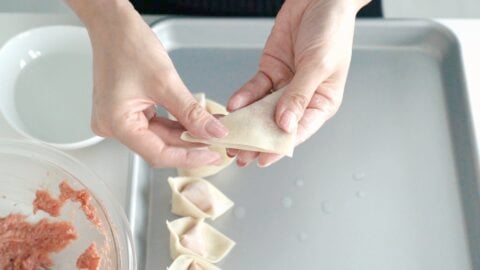 Folding pork filling into a wonton wrapper.