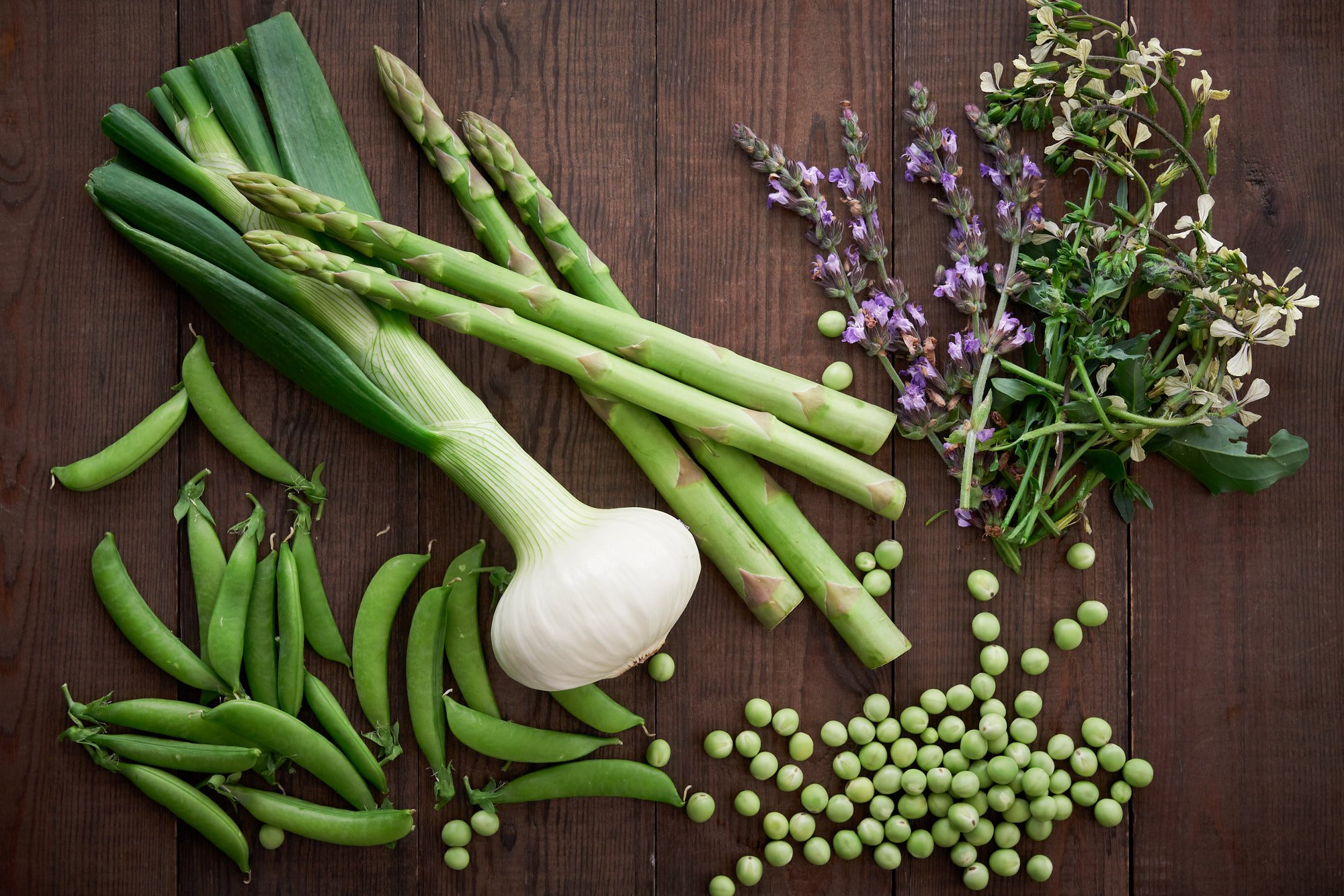 Snap peas, asparagus, sage flowers, arugula flowers, and green peas on a wood for spring pasta.