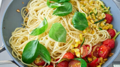 Basil and spaghettini being tossed with pan-roasted tomatoes, corn, and zucchini for Pasta Estate (Summer Pasta).