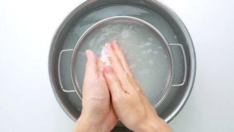 Scrubbing sushi rice with hands.