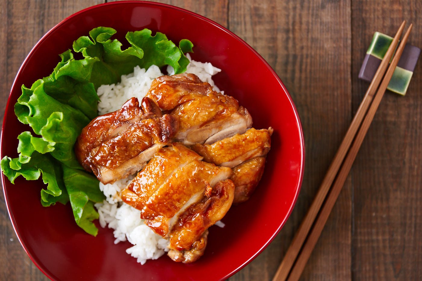 Delicious savory sweet Chicken Teriyaki in a red bowl over rice. Lean to make this easy Japanese favorite.