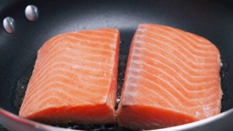 Salmon filets frying in a pan.