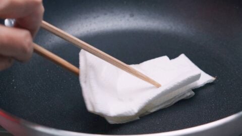 Wiping out excess oil from the pan before adding the teriyaki sauce.