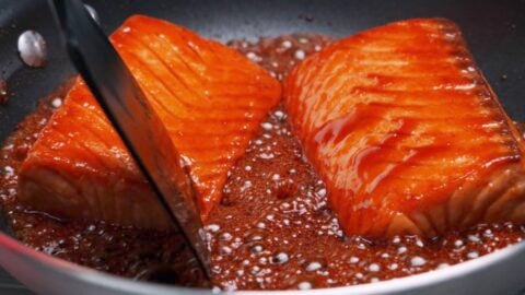 Teriyaki salmon being glazed with teriyaki sauce.