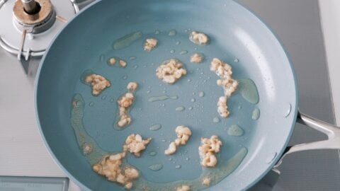 Rendering fat from chicken skin in a frying pan.