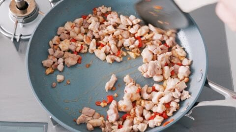 Stir-frying chicken and chilies for spicy basil chicken.