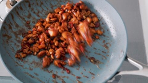 Tossing Basil Chicken with sauce in a frying pan.