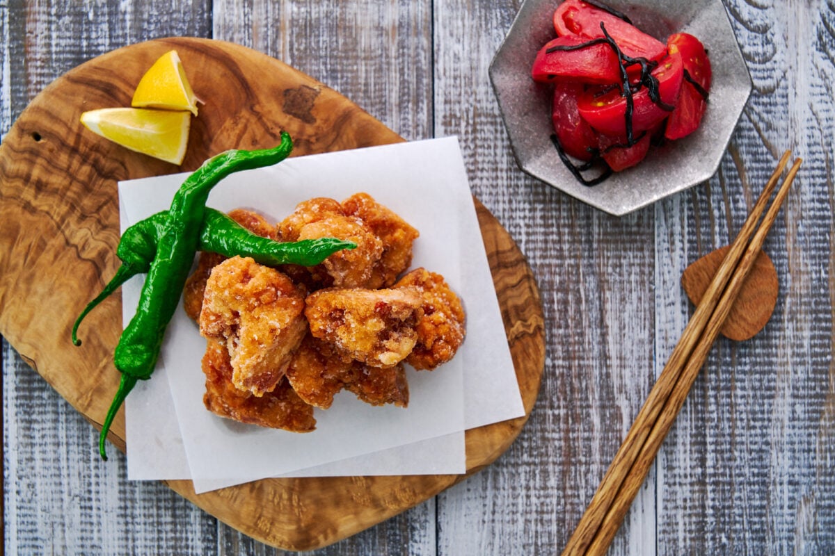 Tofu karaage (vegan Japanese fried chicken) on a sheet of paper with peppers and lemon wedges.