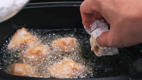 Potato starch dusted marinated tofu being added to hot oil to deep fry.