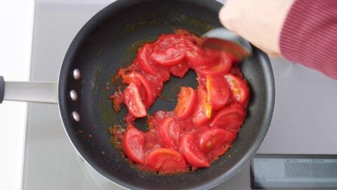 Stir-frying tomatoes in a frying pan.