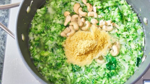 Nutritional yeast and raw cashew nuts go into a pot of chopped broccoli with vegetable stock.