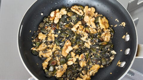 Caramelized garlic, olive oil, walnuts, pumpkin seeds, chia seeds and nigella seeds in a frying pan.