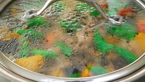 Snap peas steaming on top of Nikujaga, covered with a glass lid.