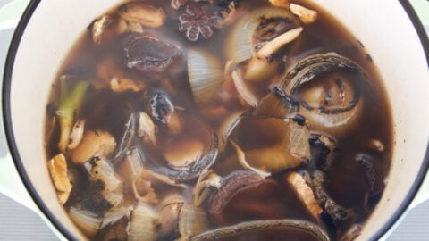 Charred aromatics and dried mushrooms simmering in a dutch oven for vegan pho recipe.