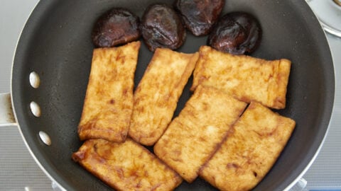 Shiitake mushrooms and fried tofu in a frying pan, glazed with vegan pho broth and hoisin sauce.