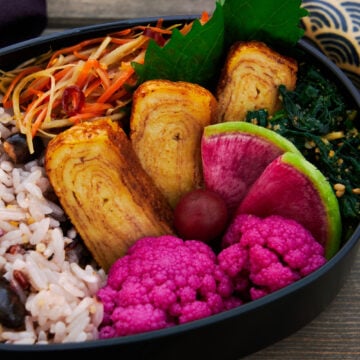 Japanese bento box lunch with vegan tamagoyaki, pickled cauliflower, sesame spinach, and stir-fried burdock with carrots.