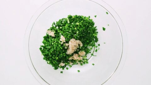 Chopped garlic chives and grated ginger in a glass bowl.